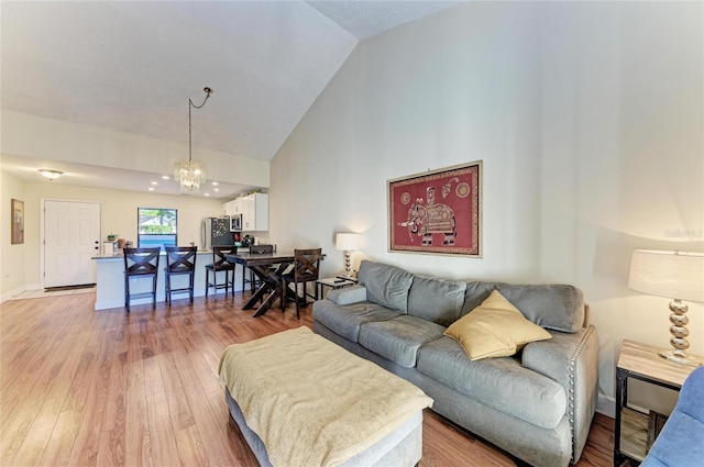 living room featuring high vaulted ceiling, a chandelier, and light wood-type flooring