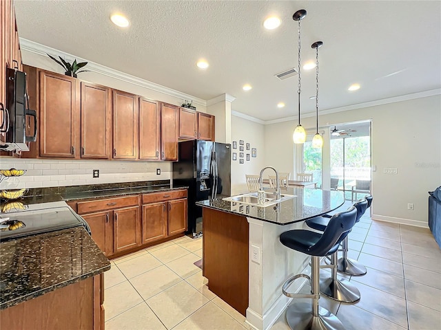 kitchen with pendant lighting, sink, light tile patterned floors, black appliances, and a center island with sink