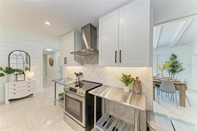 kitchen with backsplash, wooden walls, white cabinets, stainless steel electric stove, and wall chimney exhaust hood