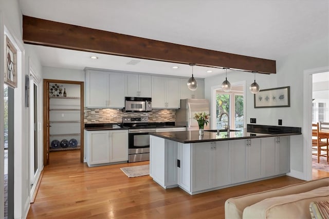 kitchen featuring stainless steel appliances, dark countertops, backsplash, light wood-style flooring, and a sink