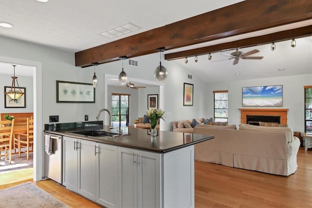 kitchen featuring decorative light fixtures, dishwasher, sink, vaulted ceiling with beams, and light hardwood / wood-style floors