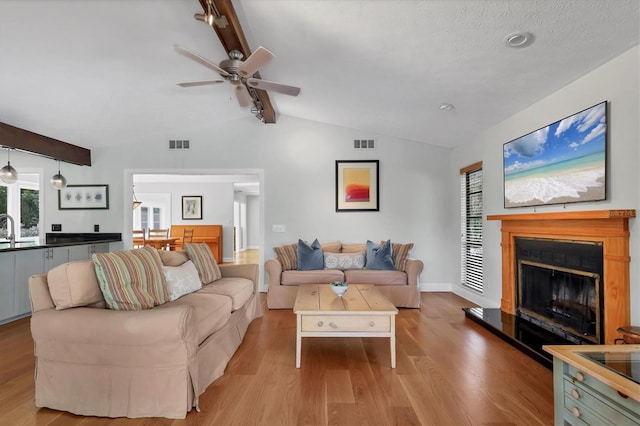 living area with lofted ceiling with beams, wood finished floors, a glass covered fireplace, and visible vents