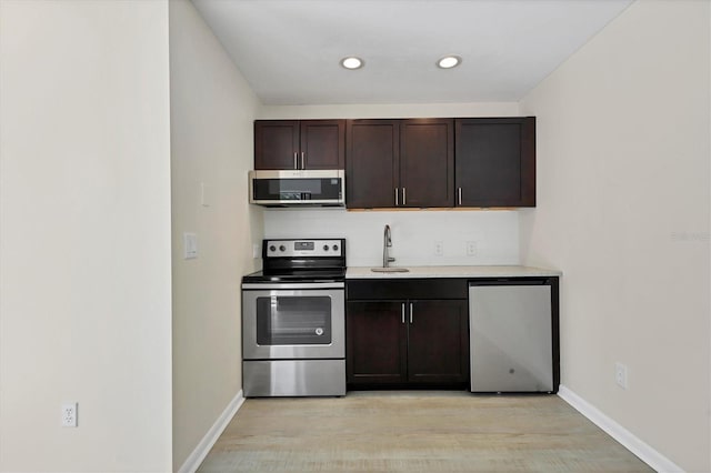 kitchen with light wood-style flooring, dark brown cabinetry, stainless steel appliances, baseboards, and light countertops