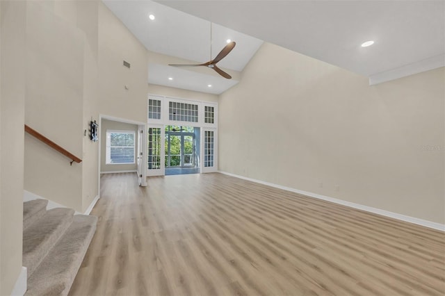 unfurnished living room featuring a high ceiling, ceiling fan, and light wood-type flooring