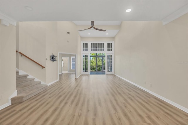 unfurnished living room with ceiling fan, a high ceiling, and light wood-type flooring