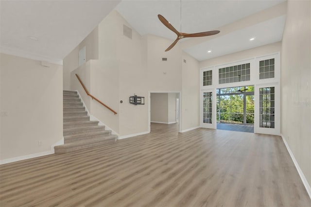 unfurnished living room featuring ceiling fan, a towering ceiling, and light hardwood / wood-style floors