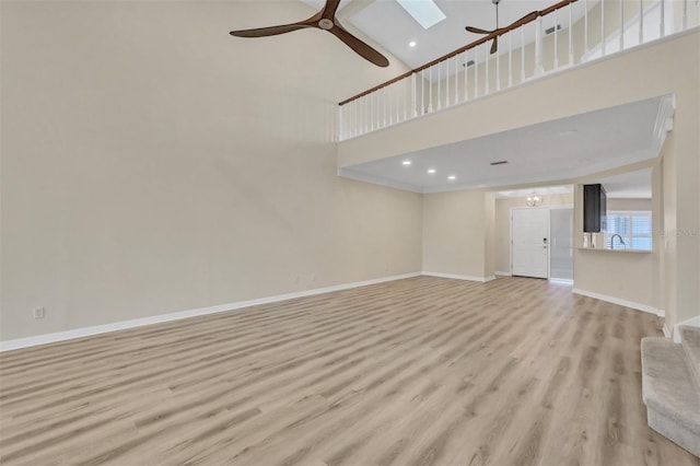 unfurnished living room with sink, a skylight, light hardwood / wood-style flooring, ceiling fan, and a high ceiling