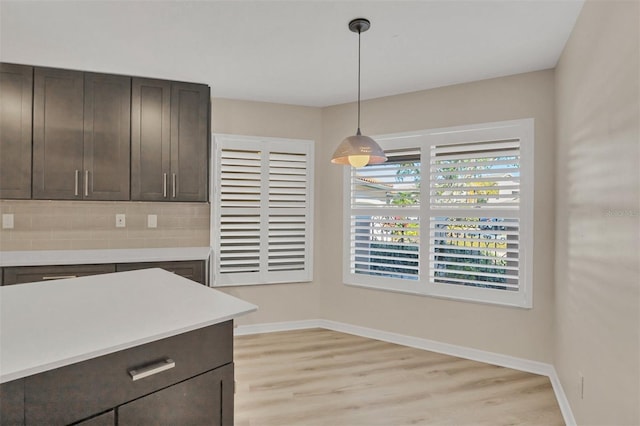 kitchen featuring dark brown cabinetry, decorative light fixtures, decorative backsplash, and light wood-type flooring