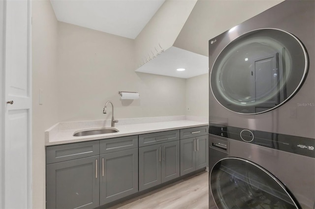 laundry room with cabinets, stacked washer and dryer, sink, and light hardwood / wood-style flooring