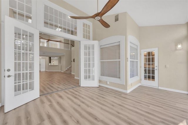 empty room featuring french doors, ceiling fan, a towering ceiling, and light wood-type flooring