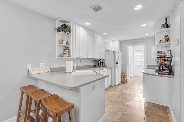 kitchen featuring open shelves, a breakfast bar, white fridge with ice dispenser, white cabinets, and a sink