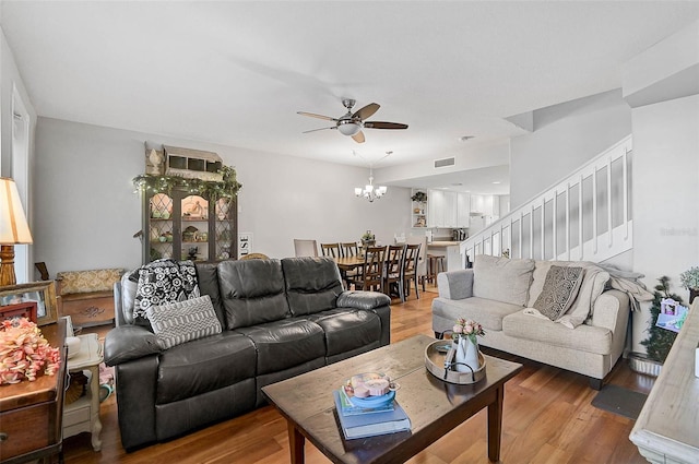 living room featuring stairs, ceiling fan with notable chandelier, wood finished floors, and visible vents