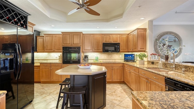 kitchen featuring a breakfast bar, a sink, black appliances, a tray ceiling, and tasteful backsplash