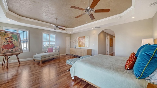 bedroom featuring arched walkways, visible vents, baseboards, a tray ceiling, and wood-type flooring