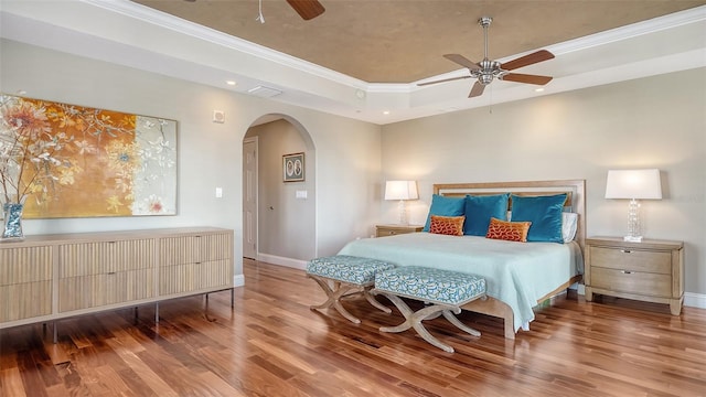 bedroom with arched walkways, a raised ceiling, visible vents, wood finished floors, and baseboards