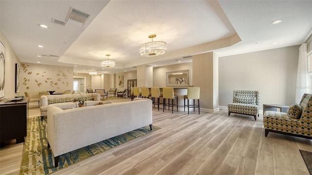 living area featuring visible vents, wood finished floors, a tray ceiling, a notable chandelier, and recessed lighting