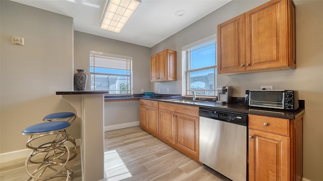 kitchen featuring light wood-style flooring, a toaster, a breakfast bar, brown cabinets, and dishwasher