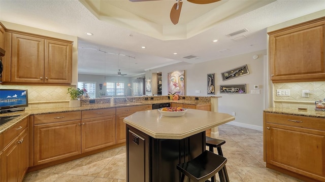 kitchen with a breakfast bar, brown cabinets, a raised ceiling, a ceiling fan, and a sink