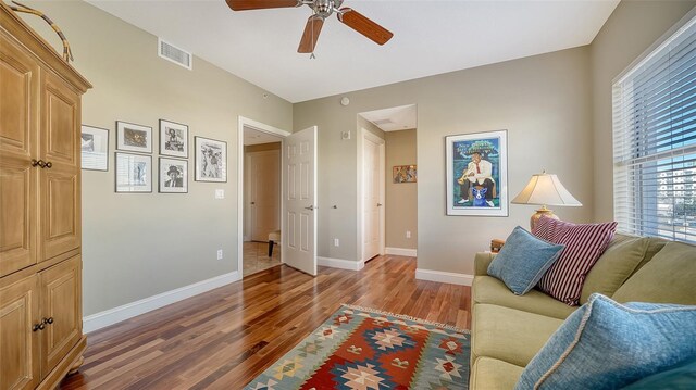 living area featuring a ceiling fan, baseboards, visible vents, and wood finished floors