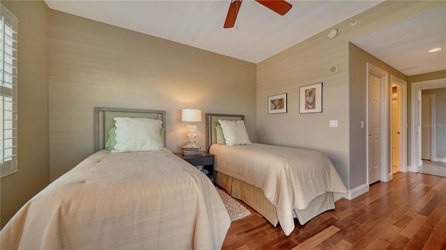 bedroom featuring a ceiling fan, multiple windows, baseboards, and wood finished floors