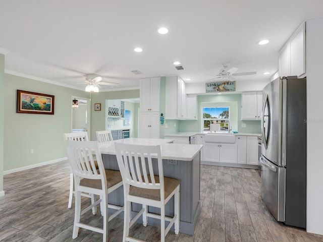 kitchen with sink, a breakfast bar, stainless steel refrigerator, white cabinets, and a kitchen island