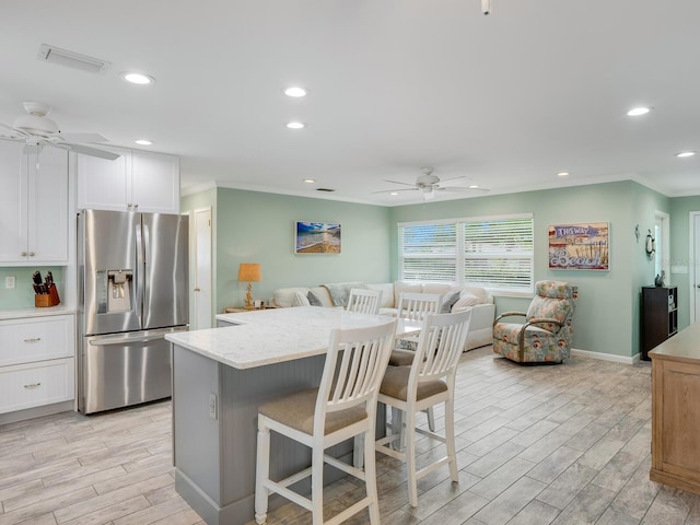 kitchen featuring ceiling fan, white cabinets, a kitchen bar, and stainless steel fridge with ice dispenser