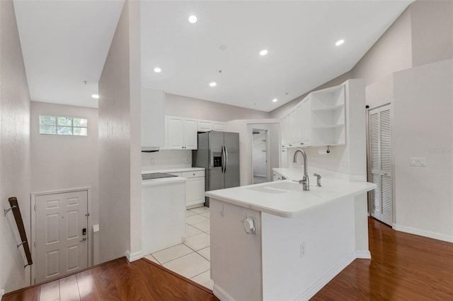 kitchen with white cabinetry, sink, stainless steel fridge, kitchen peninsula, and light wood-type flooring