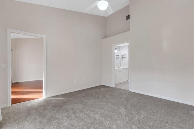 carpeted empty room featuring ceiling fan and a high ceiling