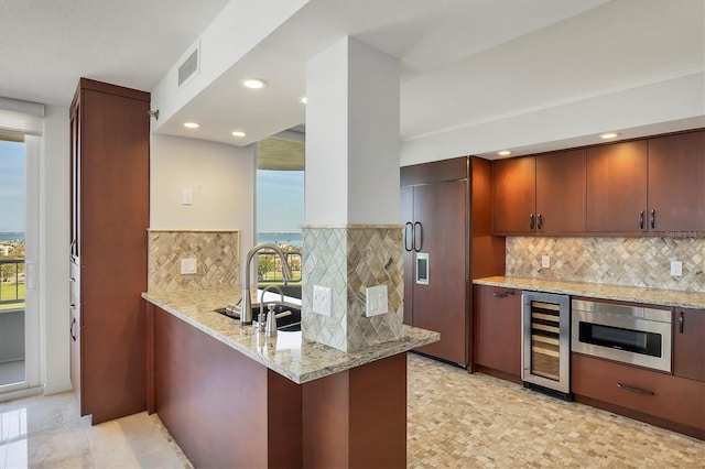 kitchen featuring paneled fridge, sink, beverage cooler, kitchen peninsula, and light stone countertops