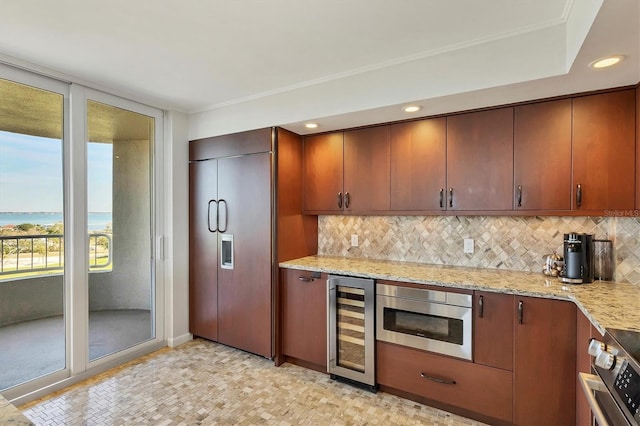 kitchen featuring tasteful backsplash, beverage cooler, built in appliances, a water view, and light stone countertops