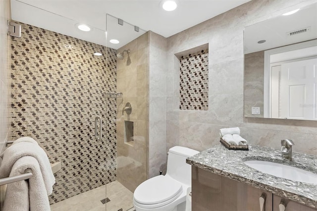 bathroom with tile walls, vanity, a shower with shower door, and toilet