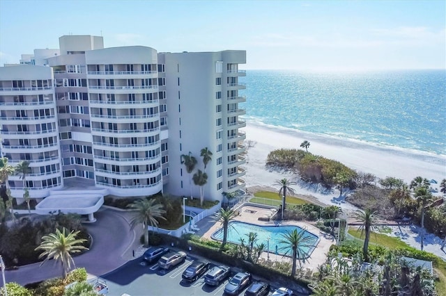 view of building exterior featuring a water view, a community pool, and a view of the beach