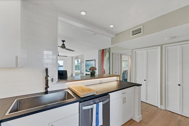 kitchen with tasteful backsplash, white cabinetry, sink, stainless steel dishwasher, and light hardwood / wood-style flooring