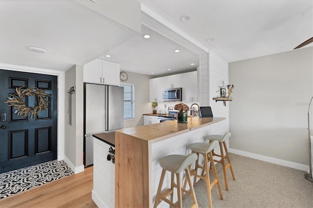 kitchen featuring a breakfast bar, wooden counters, white cabinets, kitchen peninsula, and stainless steel appliances