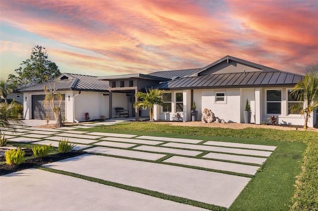 back of property at dusk with a lawn, metal roof, an attached garage, a standing seam roof, and stucco siding