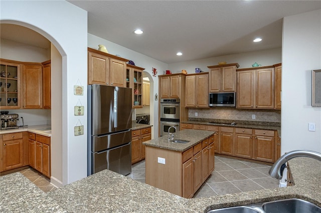 kitchen with sink, a center island with sink, light tile patterned floors, appliances with stainless steel finishes, and backsplash