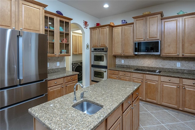 kitchen featuring stainless steel appliances, light stone countertops, sink, and a kitchen island with sink