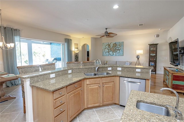 kitchen with light stone counters, dishwasher, sink, and a center island with sink