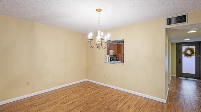 unfurnished dining area with hardwood / wood-style flooring, a textured ceiling, and a notable chandelier