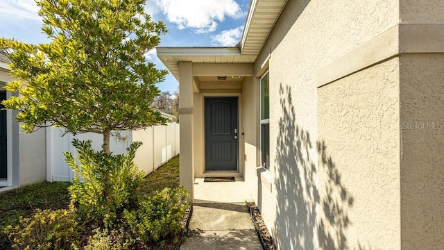 view of exterior entry with fence and stucco siding