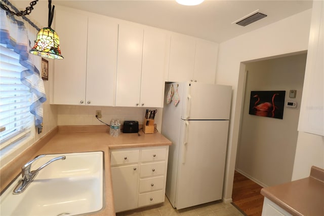 kitchen with sink, white cabinetry, hanging light fixtures, white refrigerator, and decorative backsplash