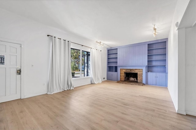 unfurnished living room with a stone fireplace, built in shelves, and light wood-type flooring