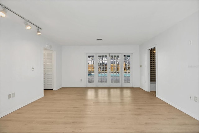 empty room featuring rail lighting, light wood-type flooring, and french doors