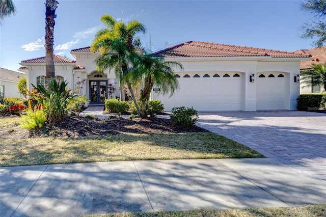 mediterranean / spanish-style house with a garage, a tile roof, decorative driveway, french doors, and stucco siding