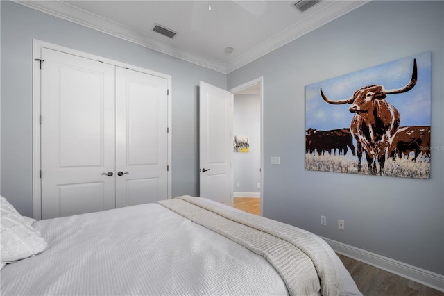 bedroom featuring wood finished floors, visible vents, baseboards, ornamental molding, and a closet