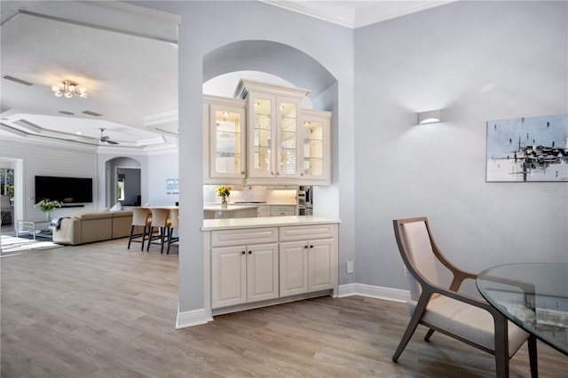 bar with arched walkways, light wood-style flooring, baseboards, ornamental molding, and tasteful backsplash