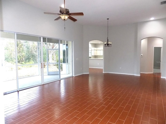 unfurnished living room with a towering ceiling, ceiling fan with notable chandelier, and dark hardwood / wood-style flooring