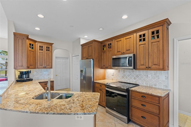 kitchen featuring stainless steel appliances, brown cabinets, a sink, and a peninsula