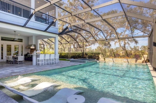 view of pool with a lanai, an outdoor bar, ceiling fan, a patio area, and exterior kitchen