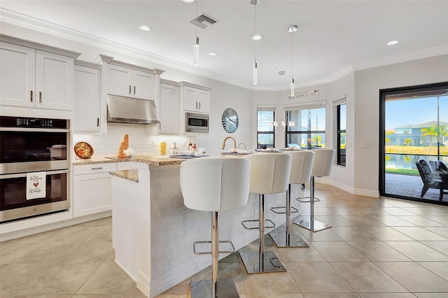 kitchen featuring a breakfast bar, a center island with sink, pendant lighting, stainless steel appliances, and light stone countertops